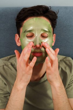 İnsan cildini yenilemek için maske takıyor. Cilt bakımı için. Evde yüz maskesi takmış rahat bir adam var.