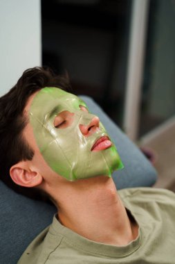 İnsan cildini yenilemek için maske takıyor. Cilt bakımı için. Evde yüz maskesi takmış rahat bir adam var.