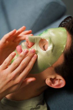 Derisini sulandırıcı ve nemlendirici yüz maskesi ile besleyip şımartıyor. Genç adam susuzluk efektli yeşil yüz maskesi kullanıyor. Erkek güzellik prosedürleri