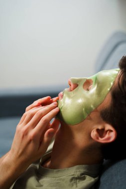 Derisini sulandırıcı ve nemlendirici yüz maskesi ile besleyip şımartıyor. Genç adam susuzluk efektli yeşil yüz maskesi kullanıyor. Erkek güzellik prosedürleri