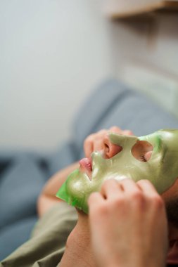 Derisini sulandırıcı ve nemlendirici yüz maskesi ile besleyip şımartıyor. Genç adam susuzluk efektli yeşil yüz maskesi kullanıyor. Erkek güzellik prosedürleri