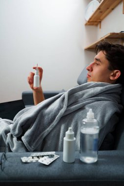 Hasta hasta sinüzit tedavisi için burun damlası alıyor. Adam evde doktor reçetesiyle ilaç ve sprey kullanıyor.