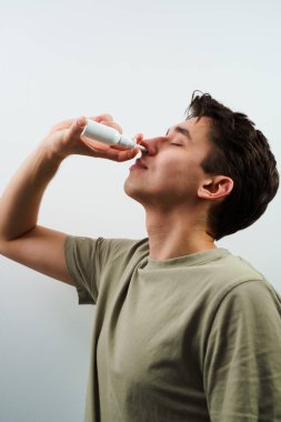 Hasta beyaz arka planda sinüzit tedavisi için burun damlası alıyor. Adam grip için burun spreyi kullanıyor.