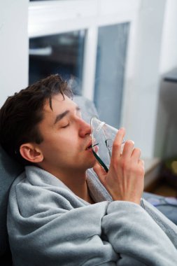 Evde öksürük tedavisi için nebulizör maskesiyle hava solumak. Hasta adam nebulizatörle solunum tedavisi görüyor.