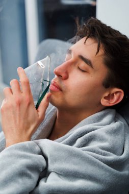 Evde öksürük tedavisi için nebulizör maskesiyle hava solumak. Hasta adam nebulizatörle solunum tedavisi görüyor.