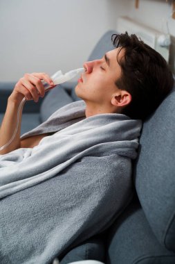 Astım krizi geçiren genç bir adam solunum cihazıyla nefes alıyor. Evde nebulizörle burun solumuş.