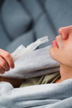 Evde nebulizörle burun solumuş. Astım krizi geçirmiş genç bir adam solunum cihazıyla nefes alıyor.