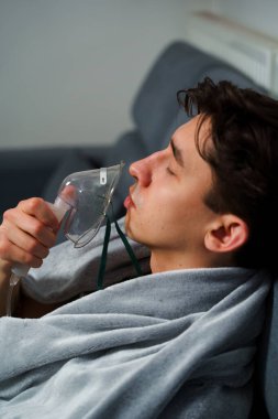 Öksürük tedavisi için oksijen maskesi yutan bir adam. Evde hastalık tedavisi için kompresör nebulizörü kullanılıyor.