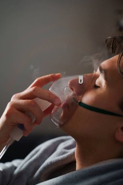 Öksürük tedavisi için oksijen maskesi yutan bir adam. Evde hastalık tedavisi için kompresör nebulizörü kullanılıyor.