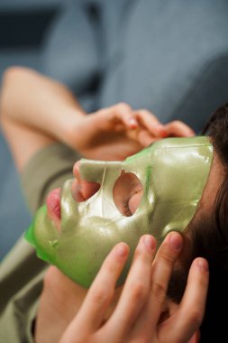 Derisini sulandırıcı ve nemlendirici yüz maskesi ile besleyip şımartıyor. Genç adam susuzluk efektli yeşil yüz maskesi kullanıyor. Erkek güzellik prosedürleri