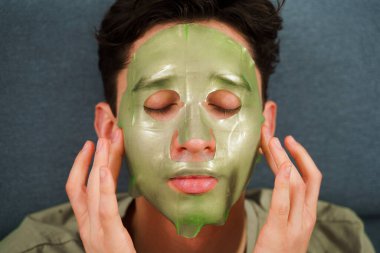 Kırışıklık önleme prosedürü ve evde yeşil maske. Adam yaşlanmayı önleyen yüz maskesi takıyor.