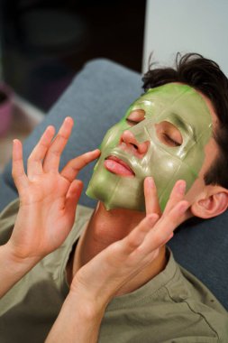 İnsan cildini yenilemek için maske takıyor. Cilt bakımı için. Evde yüz maskesi takmış rahat bir adam var.
