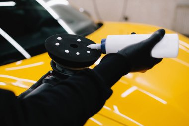 Profesyonel araba temizliği. Usta, araba gövdesini cilalamak için göz çukuru makinesine mum yapıştırıcı sürer.