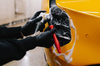 İşçi hava emme sistemini köpük ve deterjanla fırçayla temizliyor. Profesyonel araba yıkama oturumunda fırçalamak için deterjan uygulaması