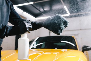Otomobil servisinde mikrofiberin üzerine mum spreyli araba temizliği. Adam detaylı işlem sırasında araba seramik cilalama için mikrofiber kumaşa balmumu ürünü püskürtür.