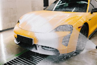 Serviste spor araba temizliği için su tabancası ile sabunlu köpük uygulaması. İşçi sabun solüsyonunu araba yıkama için su jeti basıncıyla spreyliyor
