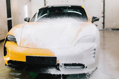 Serviste spor araba temizliği için su tabancası ile sabunlu köpük uygulaması. İşçi sabun solüsyonunu araba yıkama için su jeti basıncıyla spreyliyor