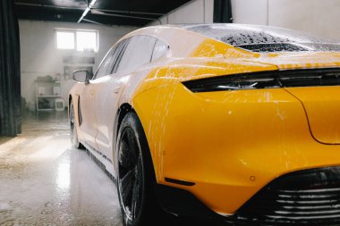 Yüksek basınçlı su tabancası detaylı temizlik için aracın yüzeyine sabun püskürtüyor. Araba yıkamada toz ve çamurdan araba temizliği.