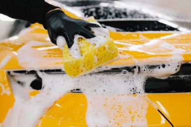 Garajda spor araba gövdesi için sarı sünger ve köpükle el yıkama. Araba yıkama makinesi oto yıkama servisinde elle köpük yıkıyor.