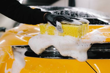 Garajda spor araba gövdesi için sarı sünger ve köpükle el yıkama. Araba yıkama makinesi oto yıkama servisinde elle köpük yıkıyor.