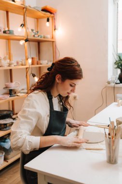Kadın esnaf seramik stüdyosunda çömlek aletleriyle killeri dikkatlice sarar. İşçi çamuru merdaneyle biçimlendirir
