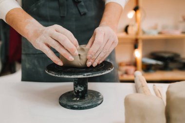 Sanatçı seramik kaseyi çömlekçi tekerleği kullanarak yontuyor. El sanatları atölyesinde kilden yemek yapıyorlar.
