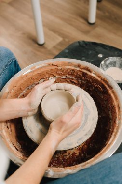 Sanatçı kadın çömlek atölyesinde porselen kaplar yapıyor. Zanaatkar dönen tekerleğin üzerinde bir çömlek tabağı yontuyor.