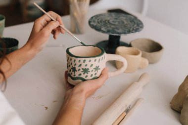 Sanatçı, fırın yangınından sonra kil seramik bardakta süsleme yapıyor. Geleneksel desenli toprak kapları tasarla