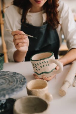 Potter, soyut bir tasarımı toprak kaplara çizer. Deneyimli ressam çömlekçilik atölyesindeki seramik bardak üzerine tasarım yapıyor.