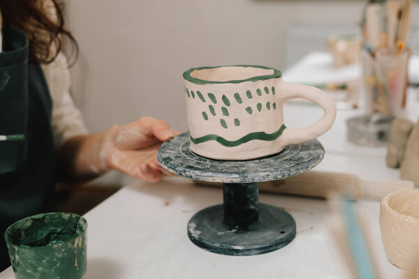 Художник рисует и делает красочное украшение глиняной посуды. Художница рисует глиняную посуду кистью и акварелью в мастерской