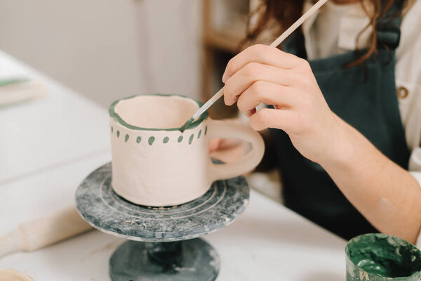 Художник украшает и рисует вручную керамические чашки глины в творческой мастерской. Художник рисует и добавляет уникальные конструкции в глиняную посуду