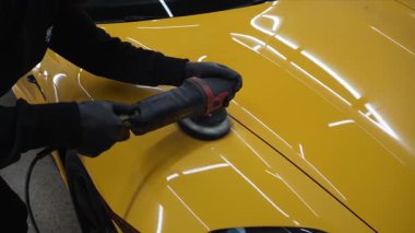 Araba servisi 4k videosunda yörüngesel cilalama makinesi kullanarak sarı spor arabanın kaput yüzeyini cilalama süreci. Yörüngesel cilalama ile cilalamak için aşındırıcı macun kullanılıyor.