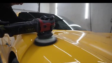 Yörüngesel cilalama ile cilalamak için aşındırıcı macun kullanmak 4k 'lık çizik videosunu silmek için. Araba servisindeki yörünge cilası makinesini kullanarak sarı spor araba kaput yüzeyinin cilalanması süreci ayrıntılandırılıyor