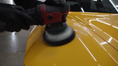 Araba servisi 4k videosunda yörüngesel cilalama makinesi kullanarak sarı spor arabanın kaput yüzeyini cilalama süreci. Yörüngesel cilalama ile cilalamak için aşındırıcı macun kullanılıyor..