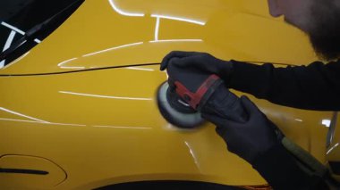 Araba servisi 4k videosunda yörüngesel cilalama makinesi kullanarak sarı spor arabanın kaput yüzeyini cilalama süreci. Yörüngesel cilalama ile cilalamak için aşındırıcı macun kullanılıyor..