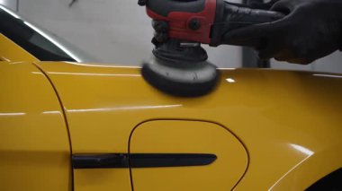 Yörüngesel cilalama ile cilalamak için aşındırıcı macun kullanmak 4k 'lık çizik videosunu silmek için. Araba servisindeki yörünge cilası makinesini kullanarak sarı spor araba kaput yüzeyinin cilalanması süreci ayrıntılandırılıyor