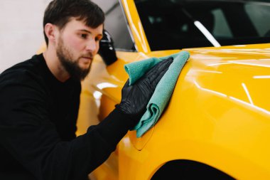 Mikro fiber silme, araba silme, cilalama ve valelik gibi titiz detaylar. Adam araba servisinde prosedürü detaylandırmadan önce arabayı mikrofiber bezle cilalıyor.