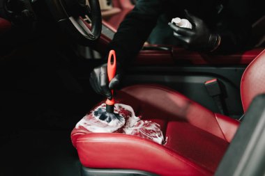 Adam, serviste detaylı işlem sırasında deri koltuğu köpük ve fırçayla temizliyor. İşçi, deri oto koltuğu için temizlik solüsyonu ve yumuşak fırça kullanır