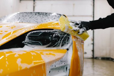 Adam sabun solüsyonu ve sünger kullanarak spor arabayı yıkar. Araba servisinde çok titiz araba detayı konsepti