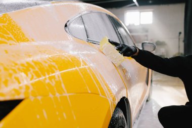 Araba yıkamadan önce sabun solüsyonuyla yıkama prosedürü. İşçi araba yıkamada arabayı süngerle temizliyor.