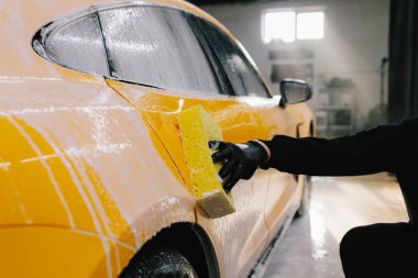 Araba yıkamadan önce sabun solüsyonuyla yıkama prosedürü. İşçi araba yıkamada arabayı süngerle temizliyor.