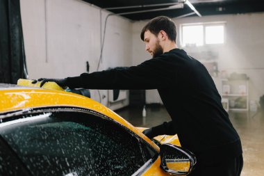 Garajda spor araba gövdesi için sarı sünger ve köpükle el yıkama. Araba yıkama makinesi oto yıkama servisinde elle köpük yıkıyor.