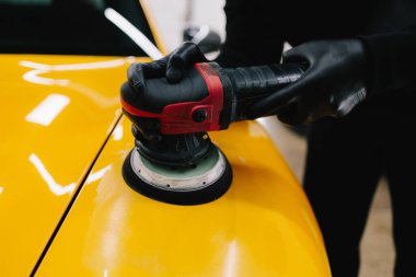 Araba servisinde yörünge cilası kullanarak sarı spor araba kaputunu cilalama işlemi. Yörüngesel cilalama ile cilalamak için aşındırıcı macun kullanılıyor.