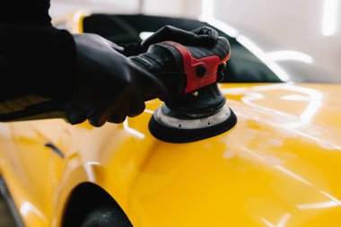 Yörünge cilasıyla cilalamak için aşındırıcı macun kullanılıyor. Araba servisindeki yörünge cilası makinesini kullanarak sarı spor araba kaput yüzeyinin cilalanması süreci ayrıntılandırılıyor