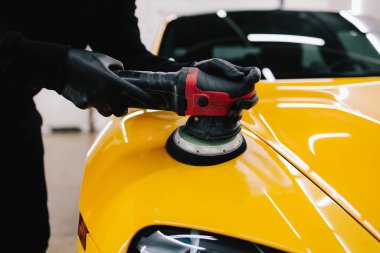 Araba servisinde yörünge cilası kullanarak sarı spor araba kaputunu cilalama işlemi. Yörüngesel cilalama ile cilalamak için aşındırıcı macun kullanılıyor.