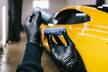 Detaylı servis çalışanı seramik koruyucu sıvıyı sünger kaplamasına uygular. Arabaya koruyucu nano katman uygulamak için şişeden süngere seramik sıvı dökme işlemi