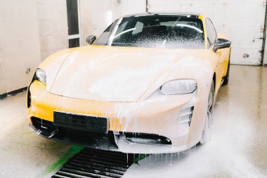 Serviste spor araba temizliği için su tabancası ile sabunlu köpük uygulaması. İşçi sabun solüsyonunu araba yıkama için su jeti basıncıyla spreyliyor