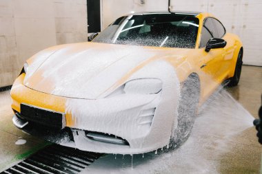 Serviste spor araba temizliği için su tabancası ile sabunlu köpük uygulaması. İşçi sabun solüsyonunu araba yıkama için su jeti basıncıyla spreyliyor