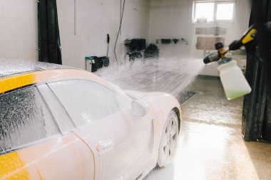 Yüksek basınçlı su tabancası detaylı temizlik için aracın yüzeyine sabun püskürtüyor. Araba yıkamada toz ve çamurdan araba temizliği.