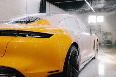 Yüksek basınçlı su tabancası detaylı temizlik için aracın yüzeyine sabun püskürtüyor. Araba yıkamada toz ve çamurdan araba temizliği.